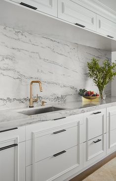 a kitchen with white cabinets and marble counter tops, gold faucet, and sink