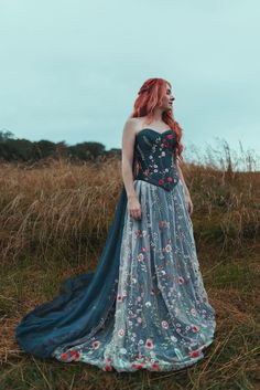 a woman with red hair wearing a blue dress and standing in the middle of a field