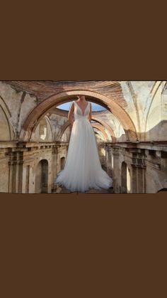 a woman in a white wedding dress standing on a stone floor with arches and arches