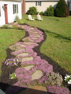 a stone path in the middle of a yard with purple flowers and white lawn chairs