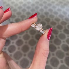 a woman's hand with red nail polish holding a diamond ring in her left hand