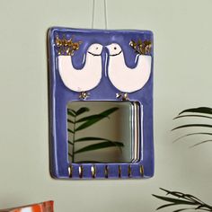 a blue and white mirror with two birds hanging from it's sides next to a potted plant