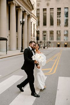 a bride and groom cross the street in front of an old building on their wedding day