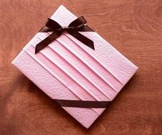 folded pink paper with black ribbon and bow on wooden table top, ready to be cut into smaller pieces