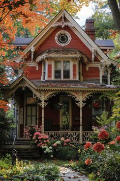 a red and white house with lots of flowers in the front yard on an autumn day