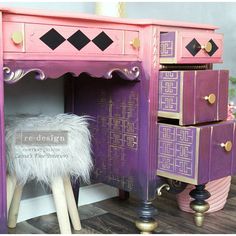 a pink and purple desk with gold trimmings on the top, sitting next to a white stool