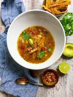 a white bowl filled with chicken tortilla soup next to sliced avocado and cilantro