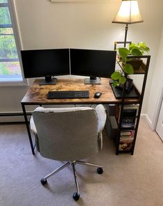 a desk with two monitors and a keyboard sitting on top of it next to a window