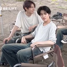 two young men sitting next to each other on top of a bench in the dirt