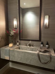 a bathroom sink sitting under a large mirror next to a vase with flowers in it