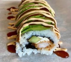 a sushi roll with sauce and avocado on it is sitting on a table