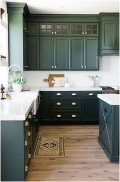 a kitchen with dark green cabinets and white counter tops, wood flooring and an area rug