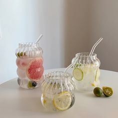 three glass vases filled with different types of drinks and fruit on top of a table