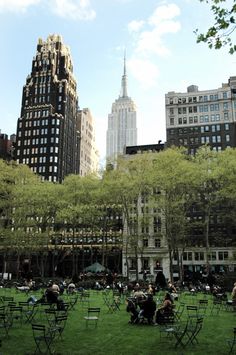 many people are sitting in the grass near tall buildings