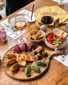 a wooden table topped with plates and bowls filled with different types of food next to glasses of wine