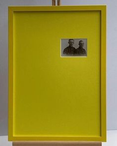 two men are standing in front of a yellow frame with a black and white photo on it