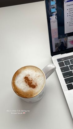 a cup of cappuccino next to a laptop computer