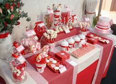 a table topped with lots of red and white desserts next to a christmas tree