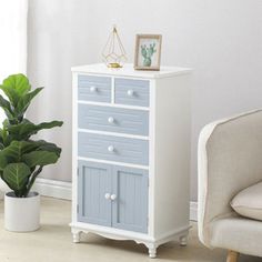 a white and blue cabinet next to a chair in a room with a potted plant