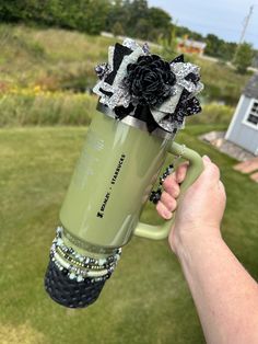 a person holding a green coffee mug with a black flower on it and some other things in the background