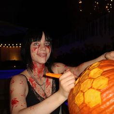 a woman holding a large pumpkin with blood all over her face and lip paint on it