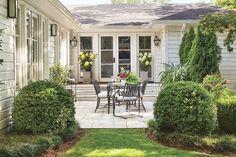 a patio with chairs, table and potted plants on the side of the house