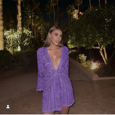 a woman in a purple dress is posing for the camera with palm trees behind her