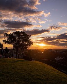 the sun is setting on top of a hill as people are standing around in the distance