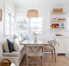 a kitchen with white walls and wooden flooring next to a dining table in front of a window