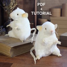 two white stuffed mice sitting on top of a wooden table next to each other,