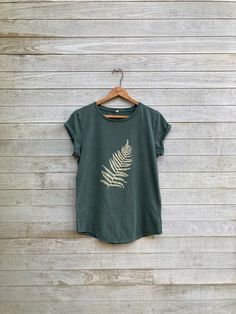 a green t - shirt hanging on a wooden wall with a fern leaf printed on it