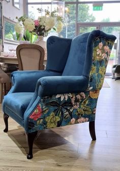 a blue chair sitting on top of a hard wood floor next to a vase filled with flowers