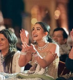 a woman sitting in the middle of a crowd clapping with her hands up and two other people standing behind her