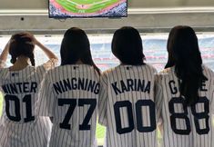 three women in baseball uniforms are looking at a television screen with the words winter karnia on it