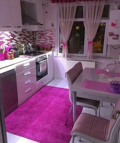 a kitchen with pink rugs and white cabinets in the center, along with a dining room table set for four