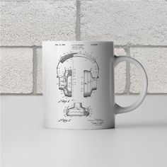 a white coffee mug sitting on top of a table next to a brick wall with drawings