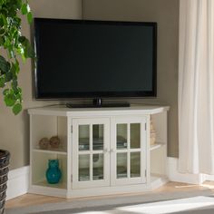 a flat screen tv sitting on top of a white entertainment center next to a potted plant