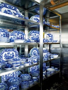 blue and white dishes are stacked on shelves in a room with stainless steel shelving