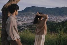 two people standing next to each other in front of a tree looking at the city