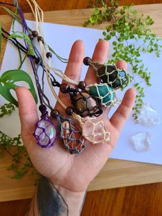 a person's hand holding several bracelets on top of a wooden table next to plants