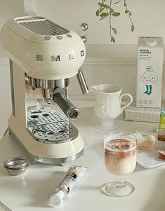 an espresso machine sitting on top of a white table next to cups and saucers