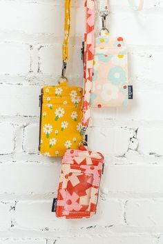 three small purses hanging on a white brick wall next to each other with flowers