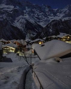 snow covered mountains and houses at night with lights shining on the buildings in the foreground