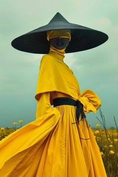 a woman in a yellow dress and black hat is standing in a field with flowers