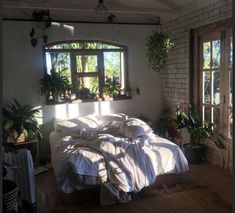 an unmade bed with white sheets and pillows in a room with potted plants