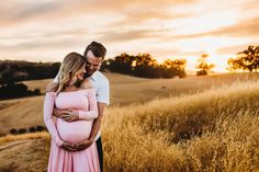 a pregnant couple standing in a field at sunset