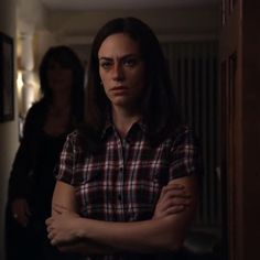 a woman standing in a hallway with her arms crossed and looking at the camera while another woman stands behind her