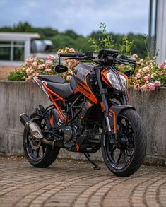 an orange and black motorcycle parked next to flowers