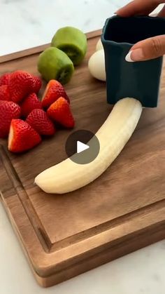 a person is cutting up fruit on a cutting board with an apple, banana, and kiwi