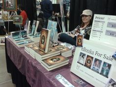 a woman sitting at a table with books for sale on it and in front of her